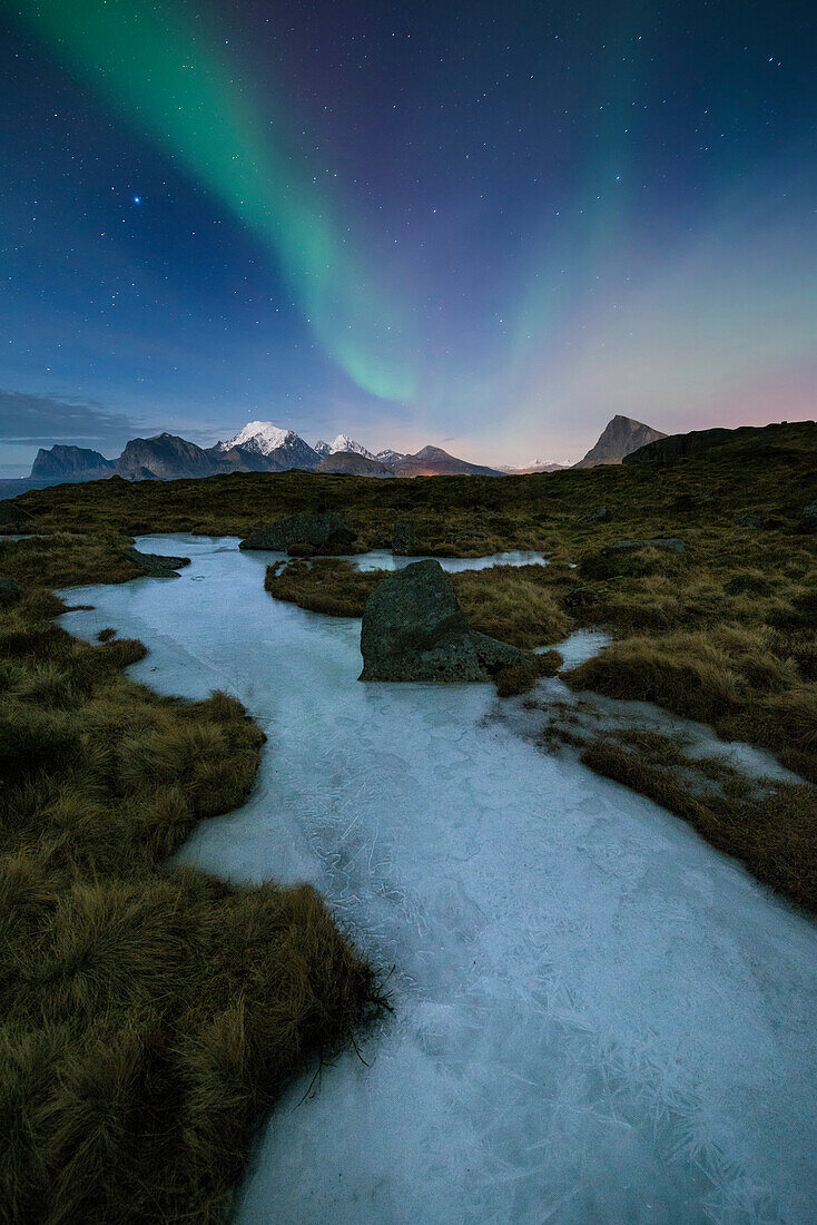 Northern Lights - Aurora Borealis shine in sky over frozen ice river and mountain landscape, Flakstad??y, Lofoten Islands, Norway
