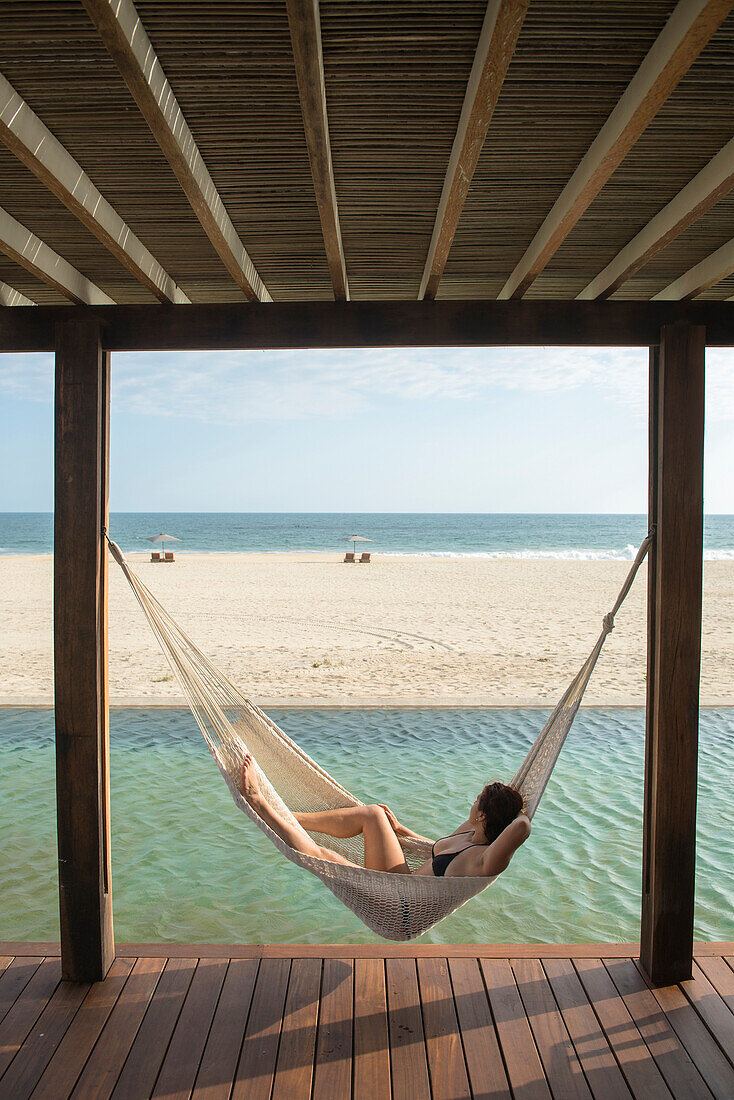 A middle age woman laying on a hamock next to a swimmng pool at a small hotel in the coast of Oaxaca, Mexico.