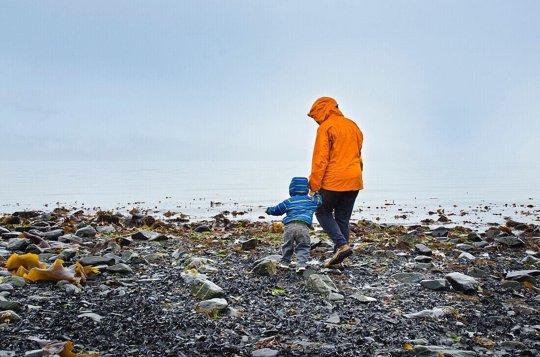 Mother and toddler exploring rocky shoreline on a rainy day in Seward, Alaska.