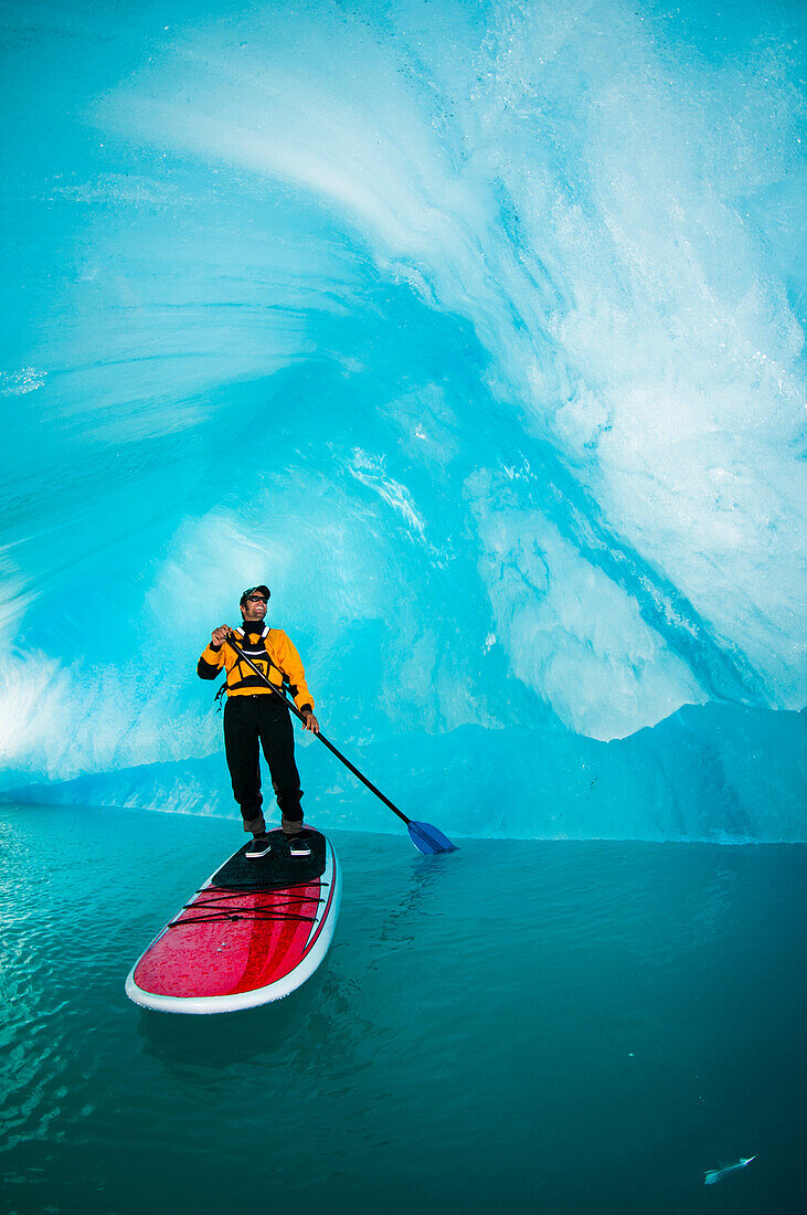 One man on stand up paddle board (SUP) maneuvers in an iceberg cavern on Bear Lake in Kenai Fjords National Park, Alaska.