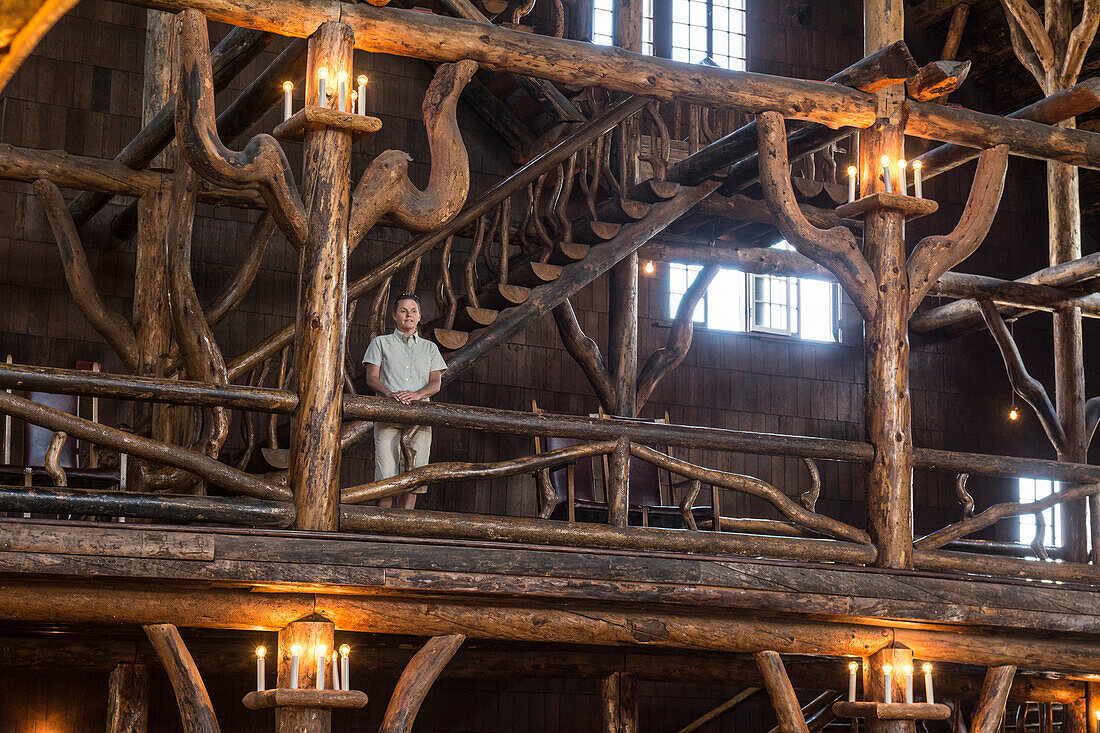 A woman standing next to the intricate logwork inside the Old Faithful Lodge in Yellowstone National Park, Wyoming.