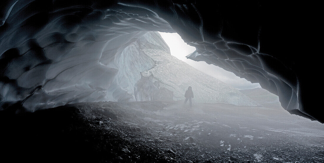 view from an icecave to a hiker standing in the steam of the geothermal springs at Hraftinnusker on the Laugavegur walking trail