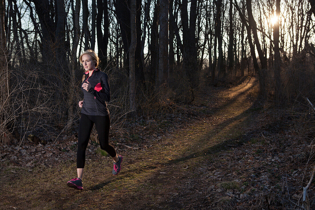 A woman runs through a wooded trail.