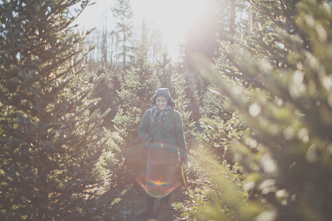 A young woman looks for the perfect tree while holding a hand saw at a local U-cut Christmas Tree farm.