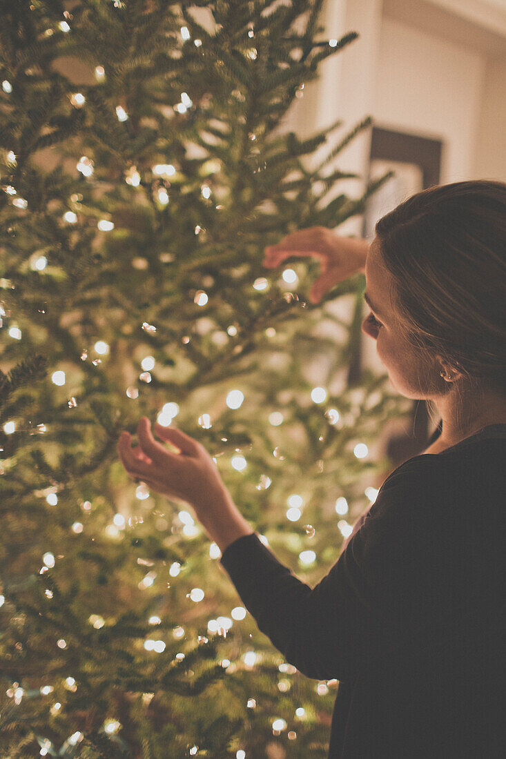 A young woman strings lights on a Christmas Tree.