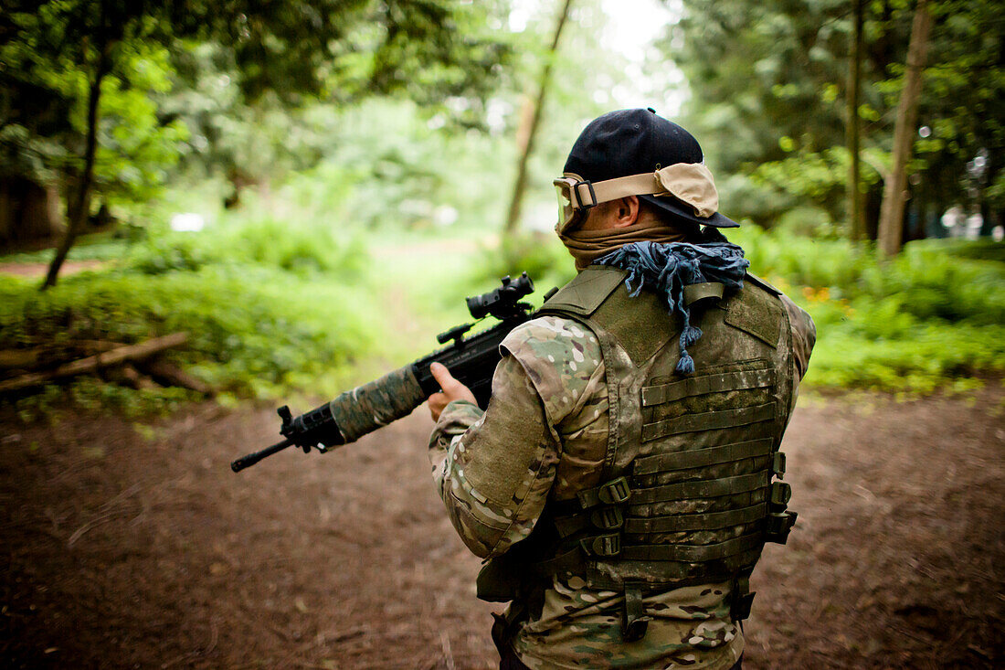 A man carries an automatic weapon while walking through the forest.