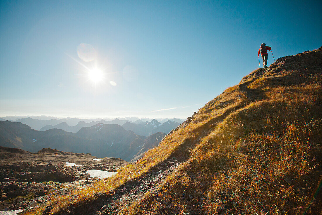 A hiker follows a footbed to the top of a mountain ridge.