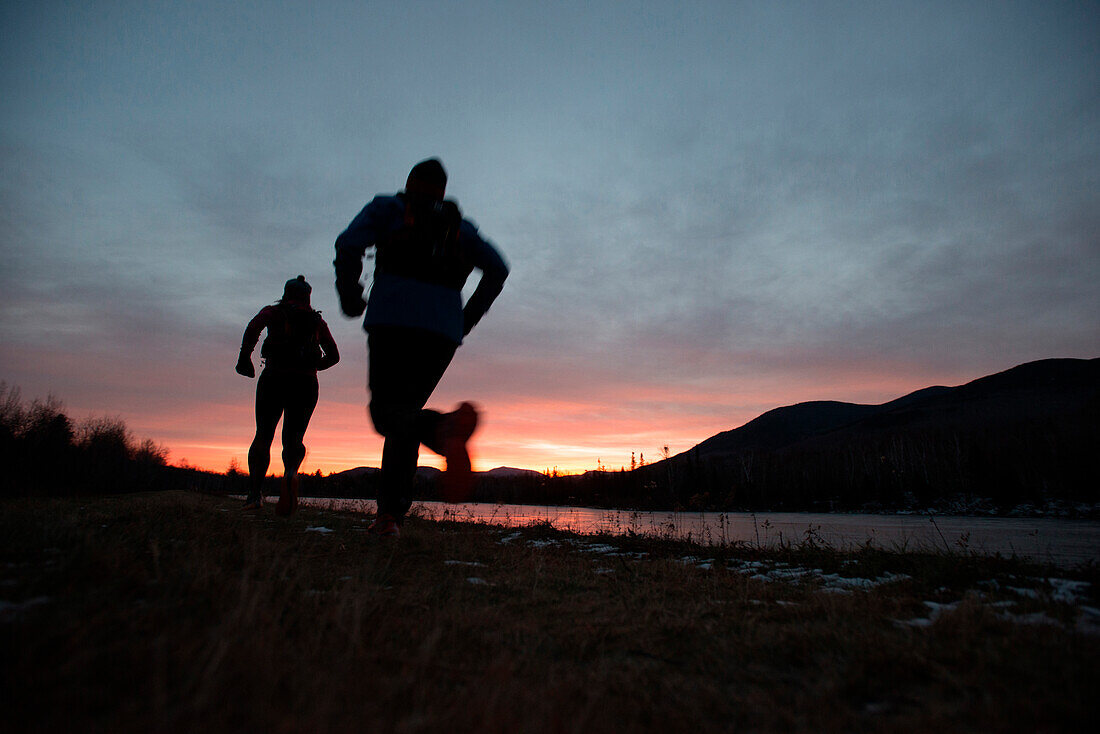 Silhouettes of two runners near Lake Durand in Randolph, New Hampshire while the sun rises on a chilly autumn morning.