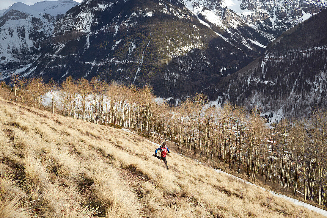 Adult male trail running through a grassy trail high in the mountains above Telluride Colorado on a beautiful spring afternoon.