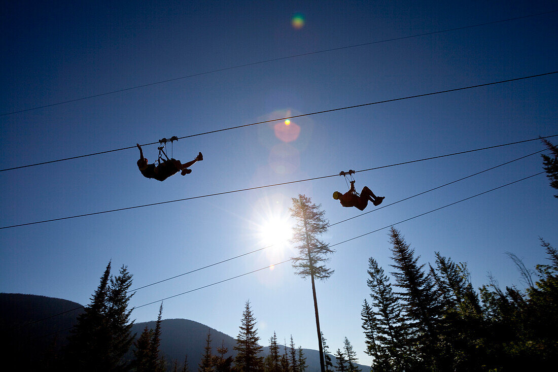 Two people ride a zip line in Whitefish, Montana.