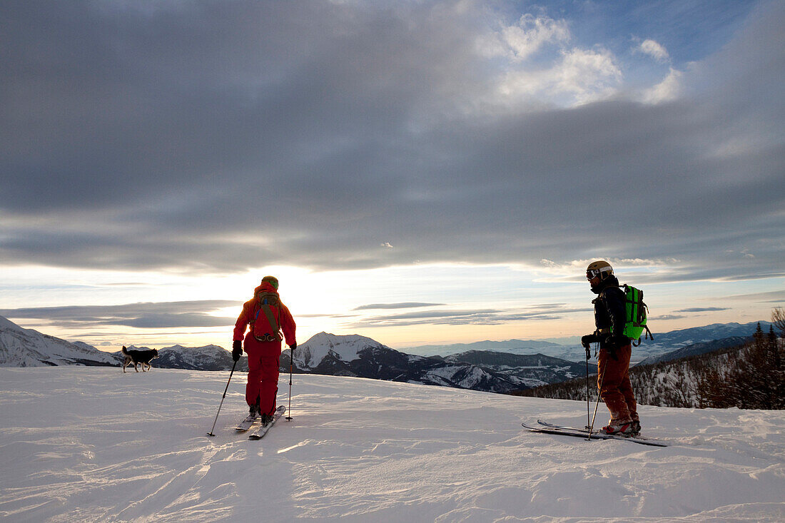 Two backcountry skiers and their dog ski across a ridge at sunset in the Beehive Basin near Big Sky, Montana.