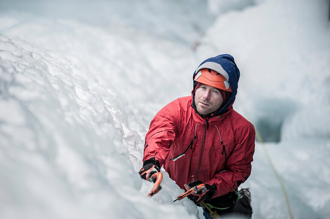 Man with red jacket and orange helmet and ice axes lead climbing an ice fall in Simplon Pass shooted from above. Valais, Switzerland.