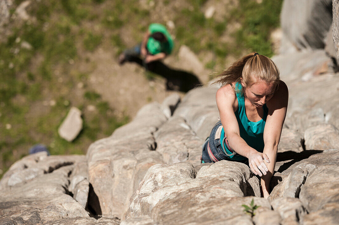 Beautiful italian blonde girl climbs a 6b crack route in Balmanolesca, the most historical granite crag in Ossola, on a sunny spring day. Varzo, Italy.