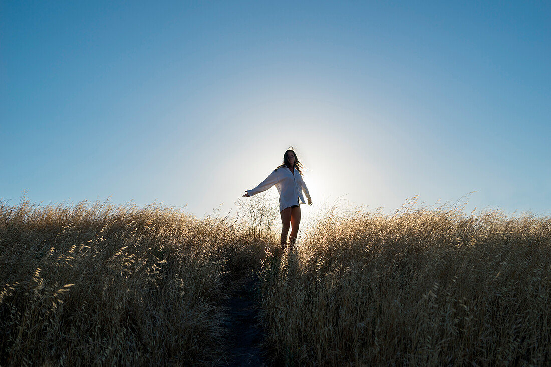 Woman dancing in a field of golden grass in sun drenched hills of California.