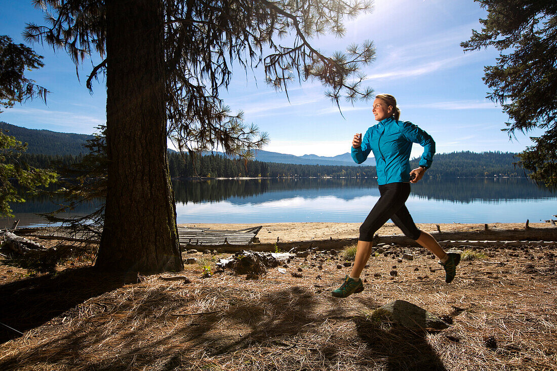 A female trail runner running next to Payette Lake in Ponderosa State Park, McCall, Idaho in the fall.