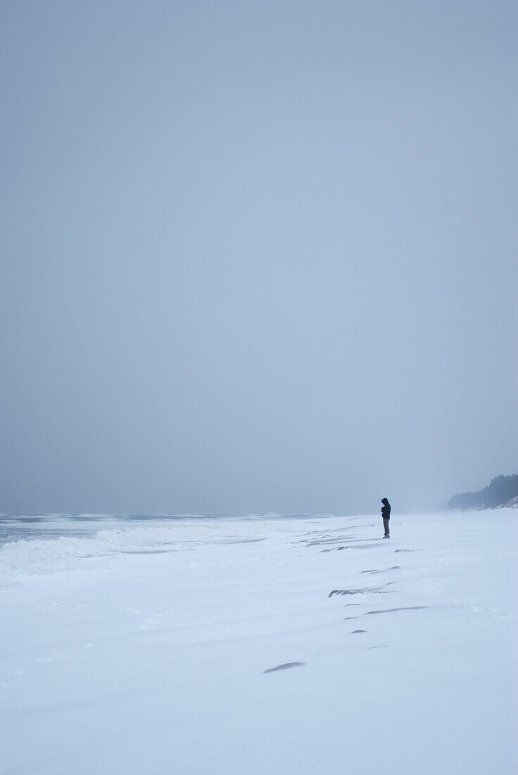 Lonely person standing on snow covered seashore.