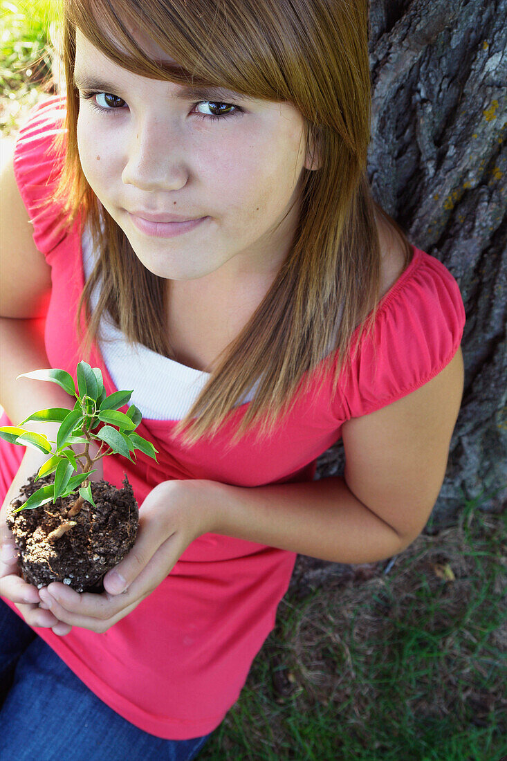 Thirteen Year Old Girl Seated Beside Tree Holding Small Tree, Winnipeg, Canada