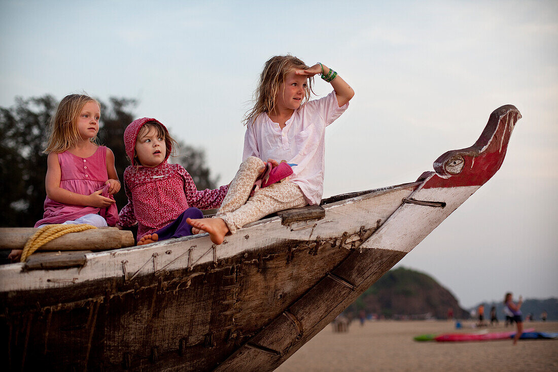 Girls play together on a traditional fishing boat on holiday in India, Patnum Beach, Goa, India.