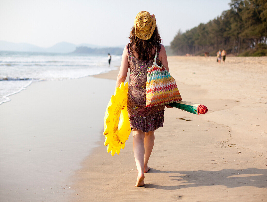 A mum walks back from beach with inflatable's and beach mat after a day on Turtle Beach, Goa, India.