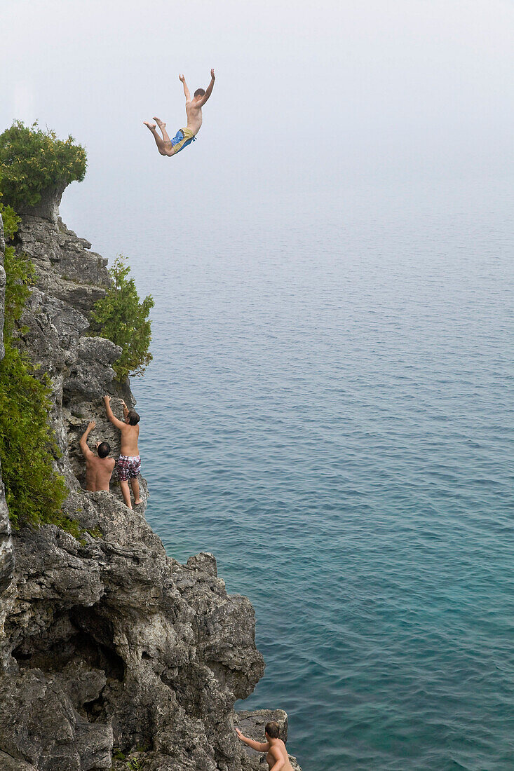 'Man leaping from a cliff into turquoise water of Georgian Bay in Bruce Peninsula National Park; Ontario, Canada'