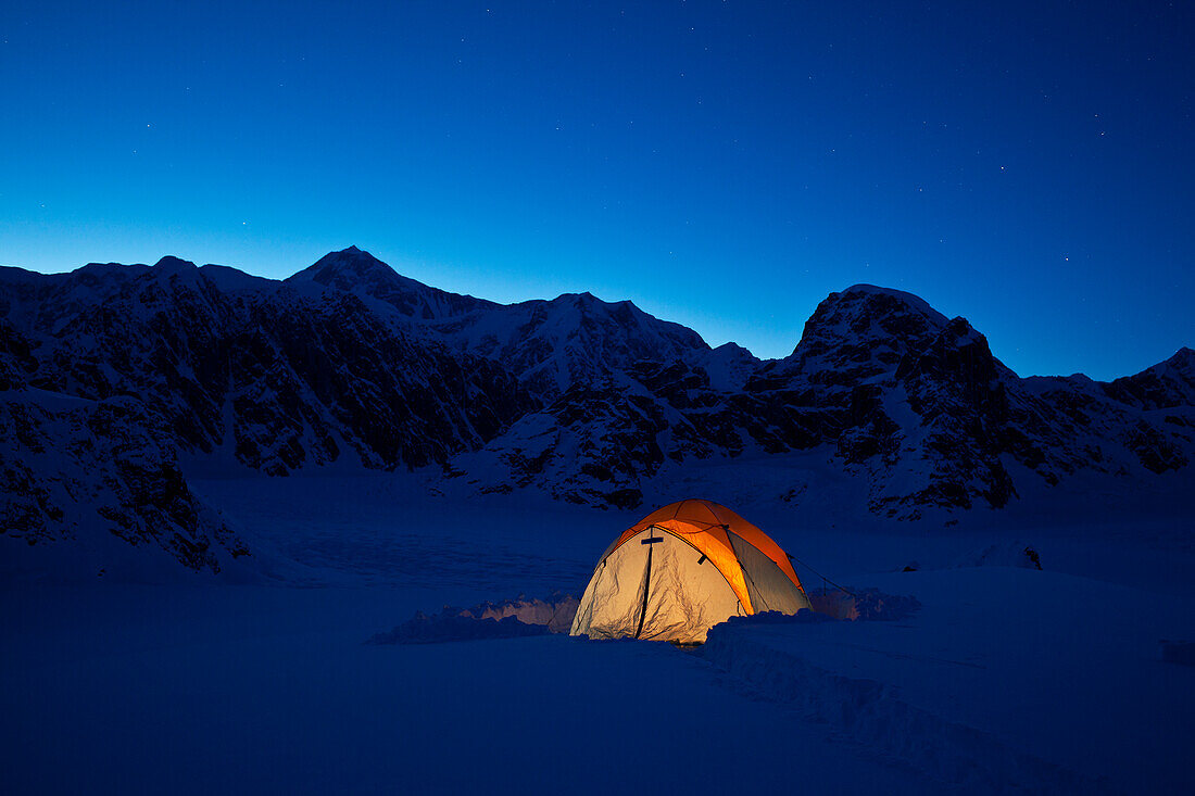 'Mountain tent on Ruth Glacier in evening, illuminated by head lamp with the summit of Mt. McKinley in background, Denali National Park and Preserve; Alaska, United States of America'