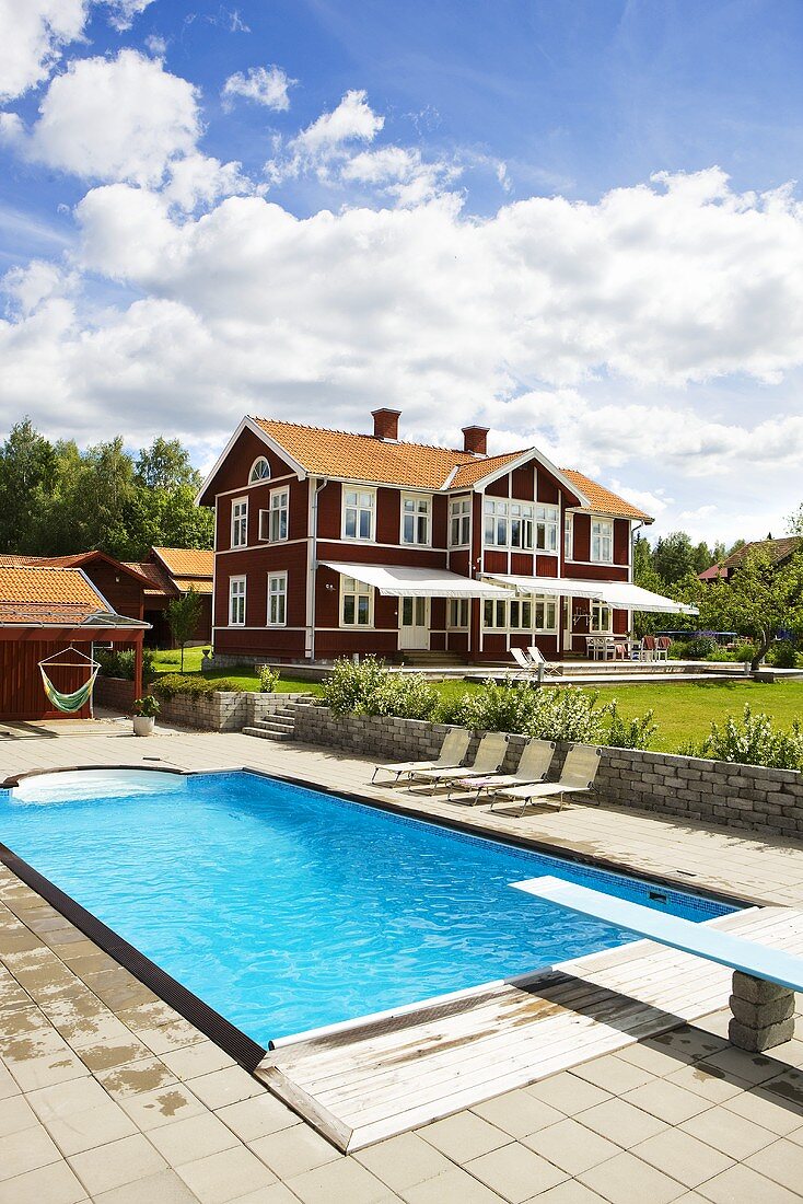 Pool with diving board and red-brown wooden house with white windows