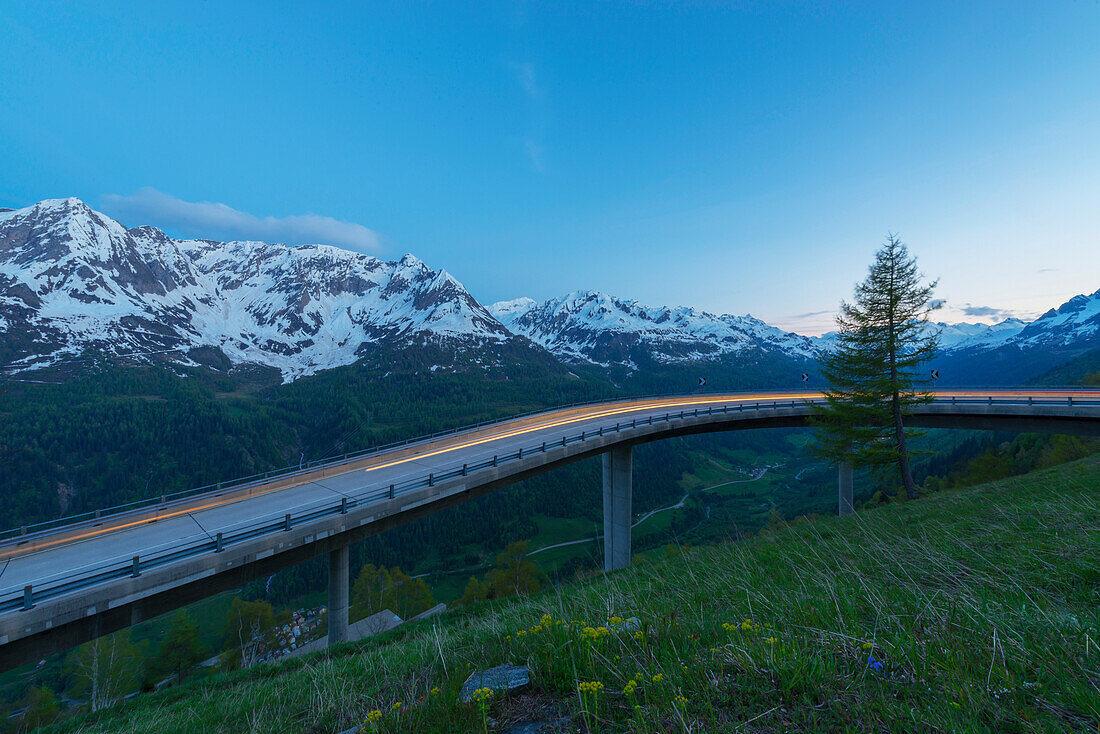 'Headlights blurred on a road with the swiss alps in the background; San Gottardo, Ticino, Switzerland'