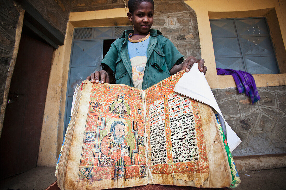 'Young boy showing an ancient bible at a church; Ethiopia'