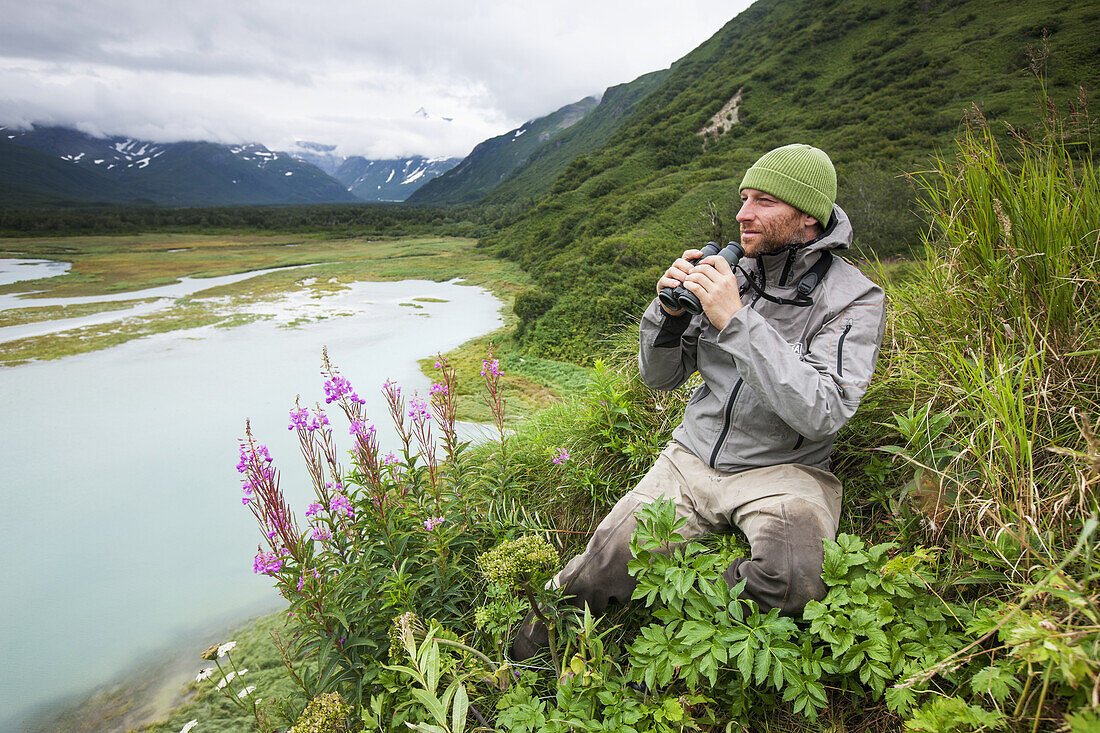 Swiss biologist and photographer glassing while sitting on a cliff overlooking Katmai Coast, Kukak Bay, Southwest Alaska