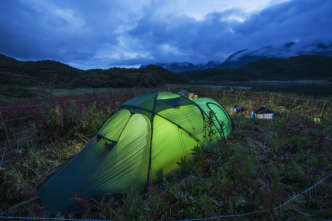 Tent glows at dusk at camp site surrounded by bear protection fence near Kinak Bay along Katmai Coast, Katmai National Park, Southwest Alaska