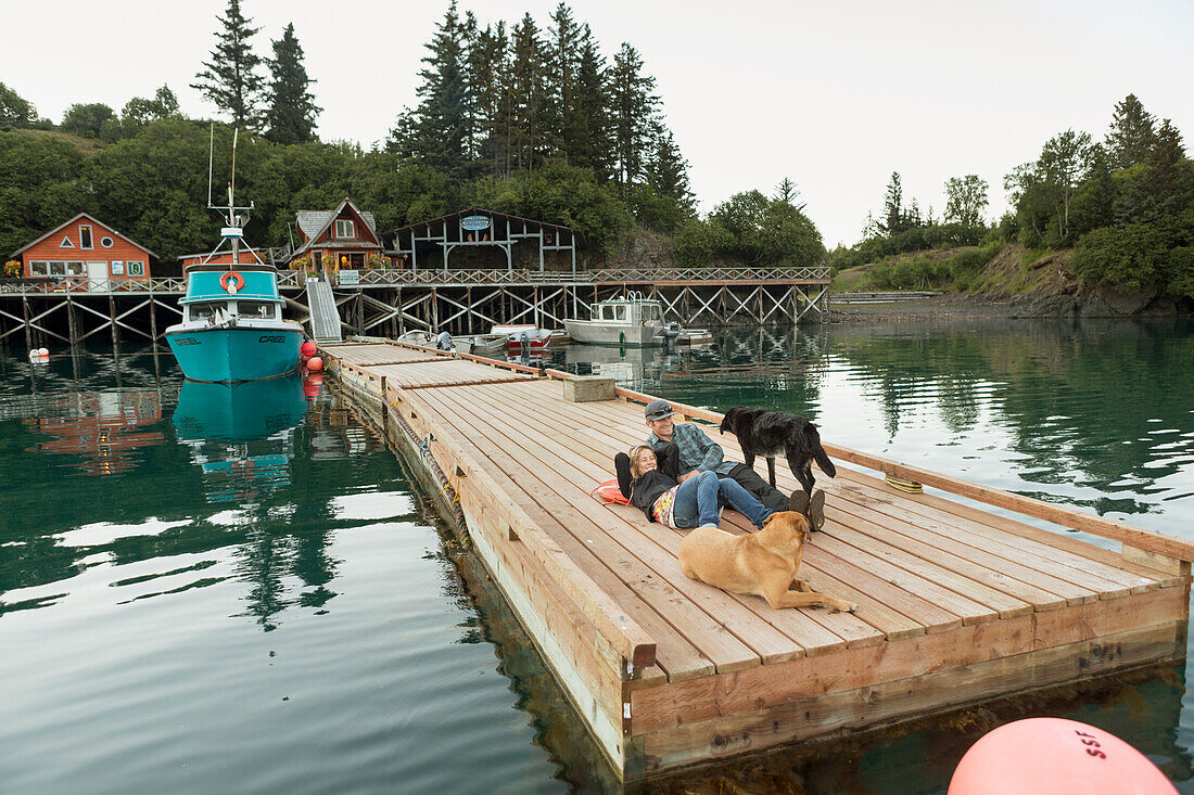 Couple relax on the dock in front of the Saltry restaurant along with two dogs, Halibut Cove, Southcentral Alaska