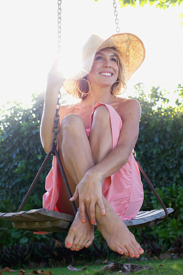 'A young woman in a strapless shirt and sunhat sitting on a swing; Kauai, Hawaii, United States of America'