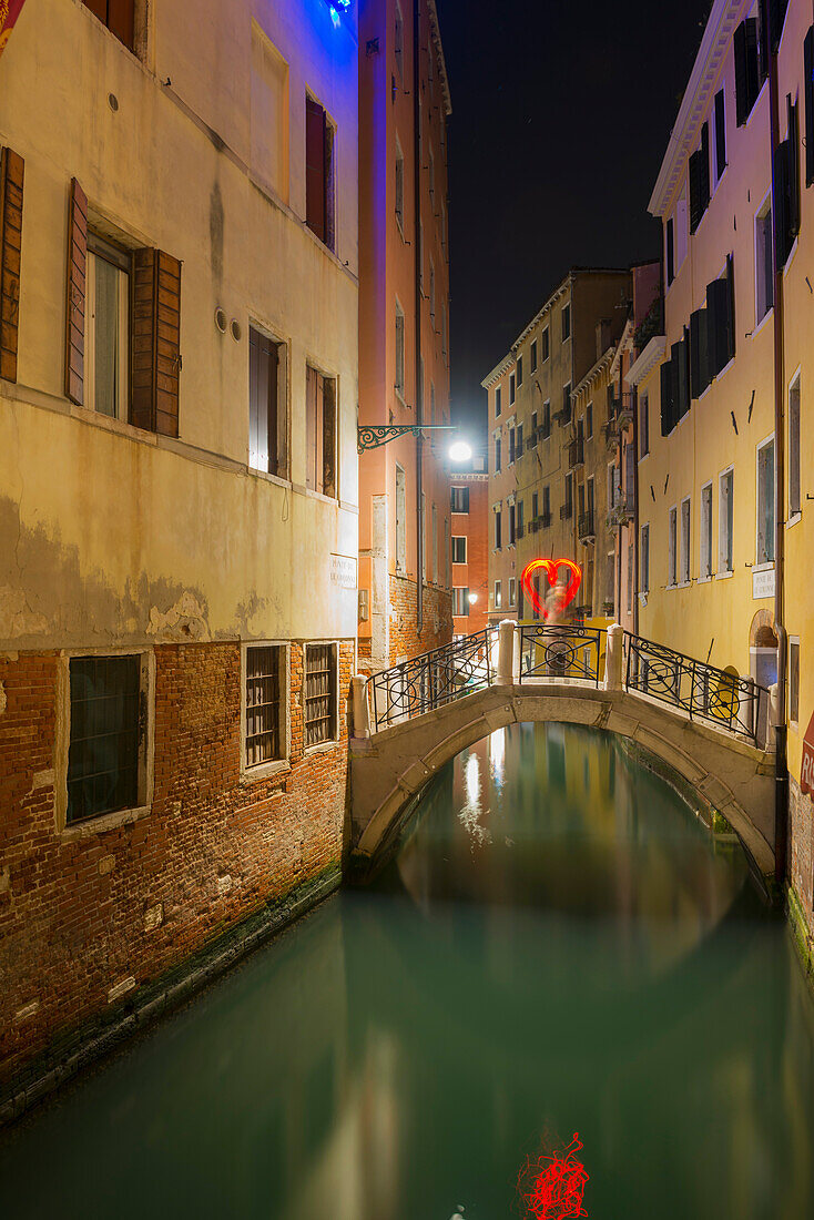 'A tranquil canal between buildings with a heart shape on a footbridge; Venice, Veneto, Italy'
