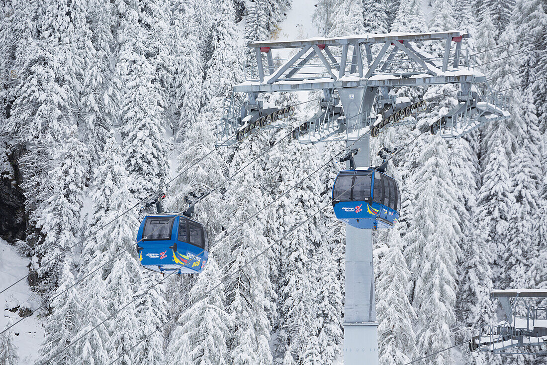 'Gondolas with tower and cables with snow covered trees on mountain slope in the background; Hintertux, Austria'
