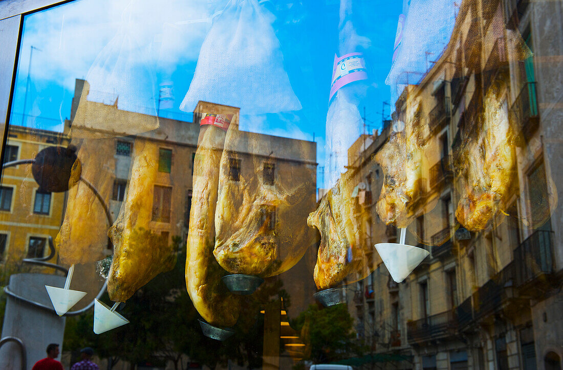 'Reflection of buildings in a window with meat hanging for sale; Barcelona, Spain'