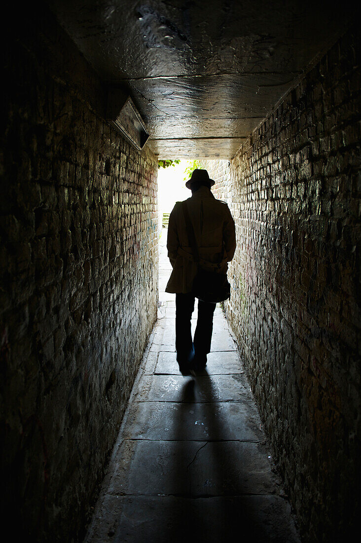 'Silhouette of a man in a top hat walking down a dark, narrow corridor; London, England'