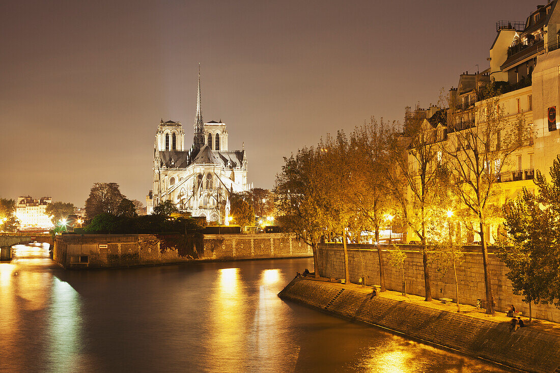 'Lights illuminate the river with an illuminated church in the background; Paris, France'