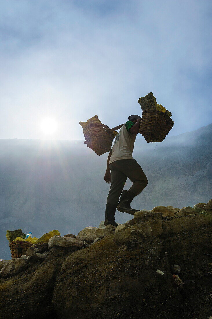 Backlit image of workers loaded with sulphur pieces cut out from a sulphur mine on Ijen crater lake, Java, Indonesia, Southeast Asia, Asia
