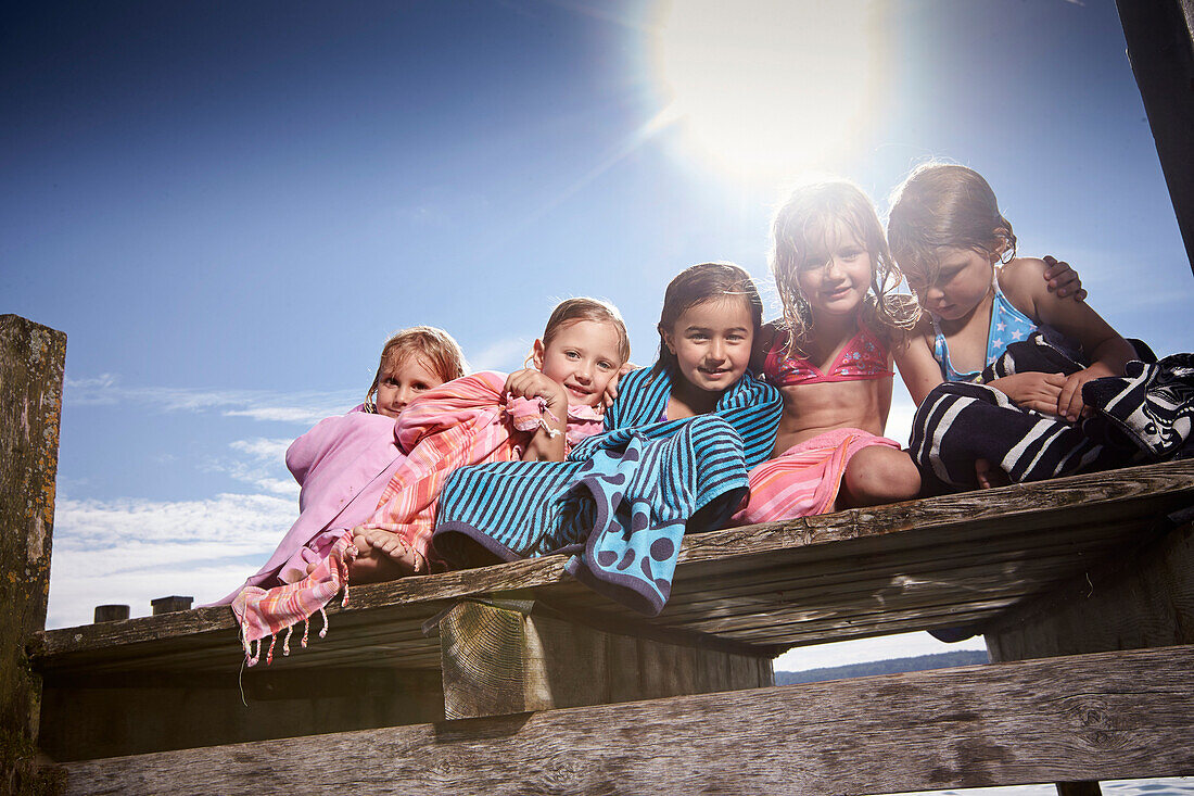 Girls sitting on a jetty, wrapped in towels, lake Starnberg, Upper Bavaria, Bavaria, Germany