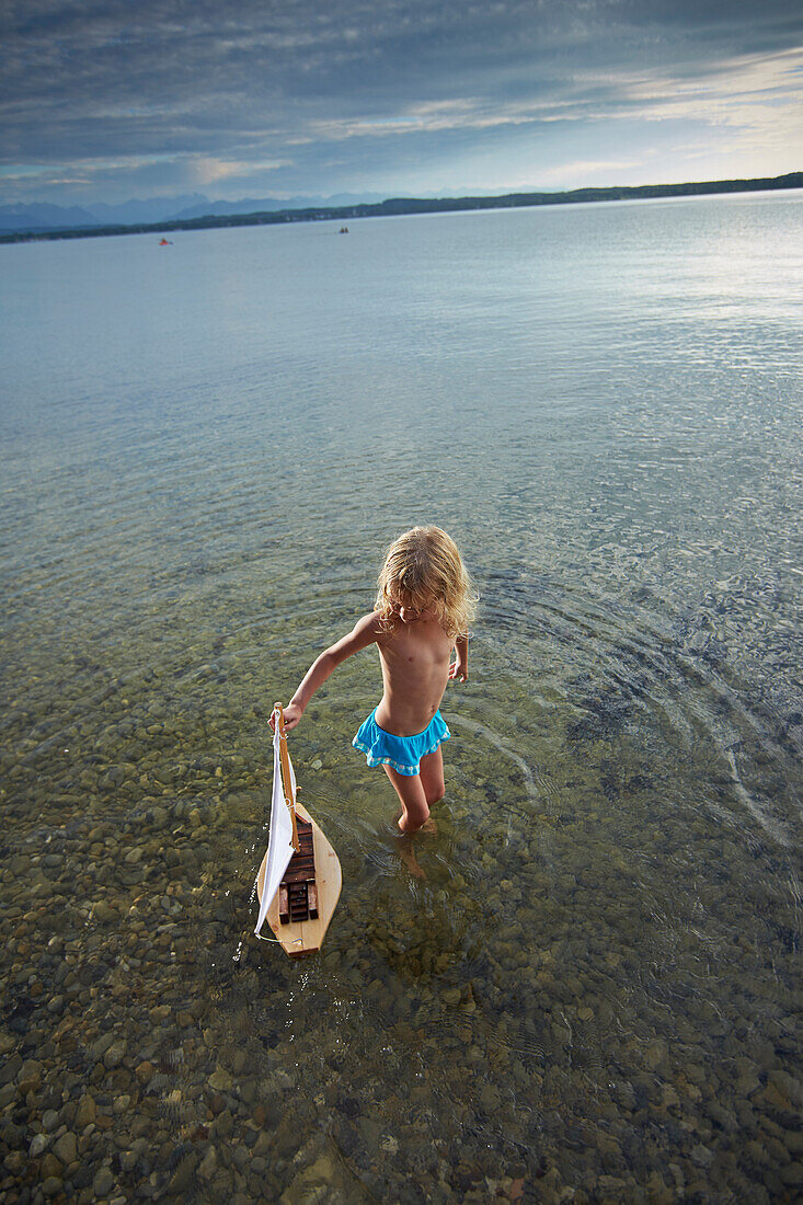 Girl with a toy sailboat in lake Starnberg, Upper Bavaria, Bavaria, Germany