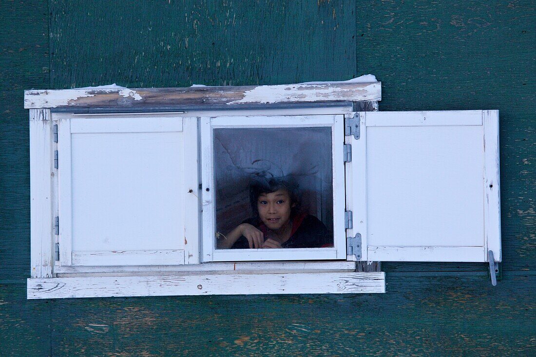 Inuit Junge schaut aus einem Fenster in Qaanaaq, Nordewest Grönland, Grönland