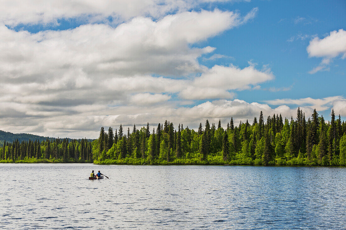 'A couple and young girl in a red canoe on Byers lake with green forested shoreline, Byers Lake Campground, Denali State Park; Alaska, United States of America'