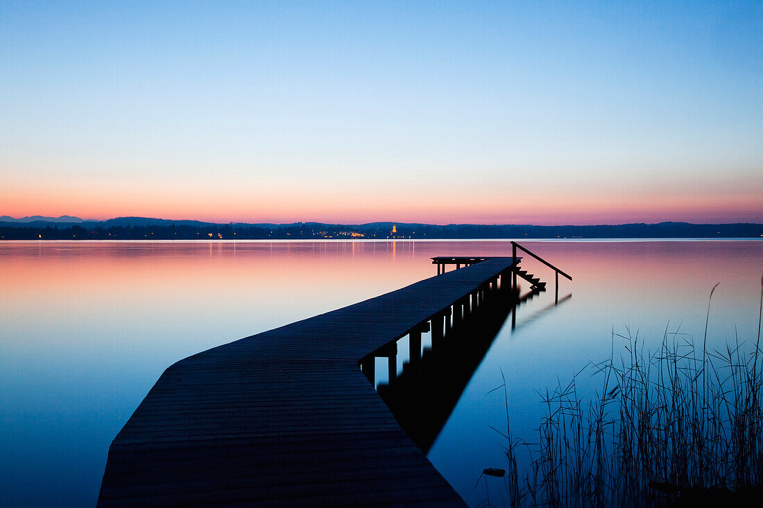 'A wooden dock leading out to a tranquil lake at sunset; Starnberger See, Bavaria, Germany'