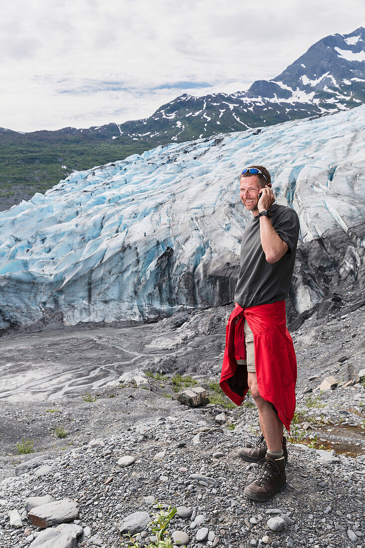'Man talking on a cell phone in front of Shoup glacier, Shoup Bay State Marine Park, Prince William Sound; Valdez, Alaska, United States of America'