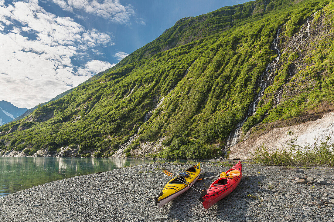 'Two kayaks on the beach in front of green mountain with waterfall at Shoup Bay State Marine Park, Prince William Sound; Valdez, Alaska, United States of America'