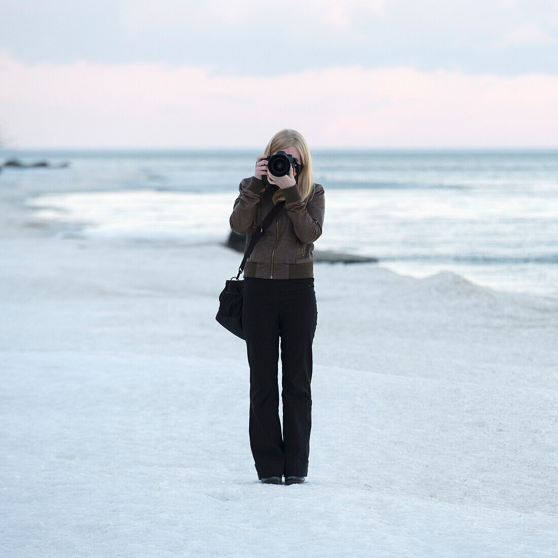 'A woman stands on the beach with a camera pointed at the camera; Riverton, Manitoba, Canada'