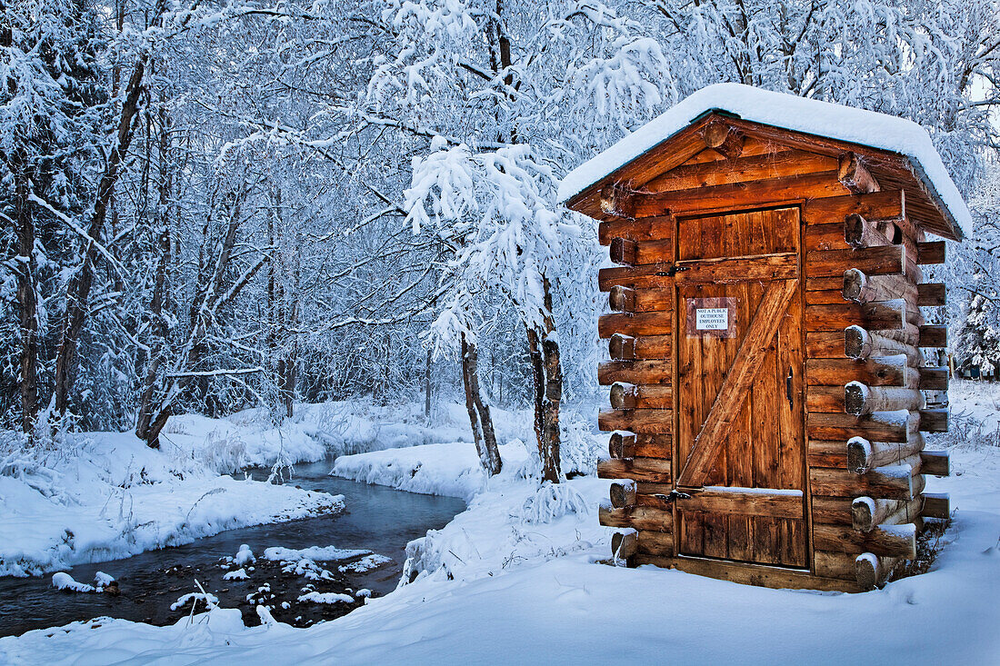 'Log outhouse by a meandering creek in snow, Chena Hot Springs Resort; Fairbanks, Alaska, United States of America'