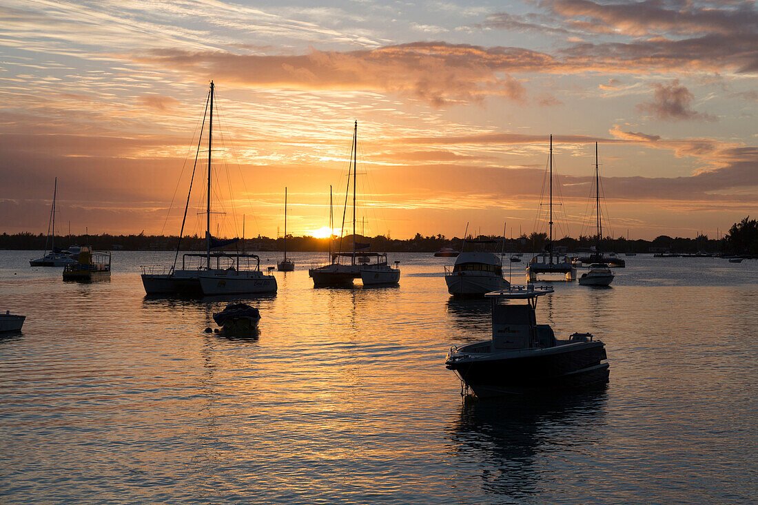 Sunset over the Indian Ocean with boats in silhouette on the calm water off the beach at Gran Baie on the north coast of Mauritius, Indian Ocean, Africa