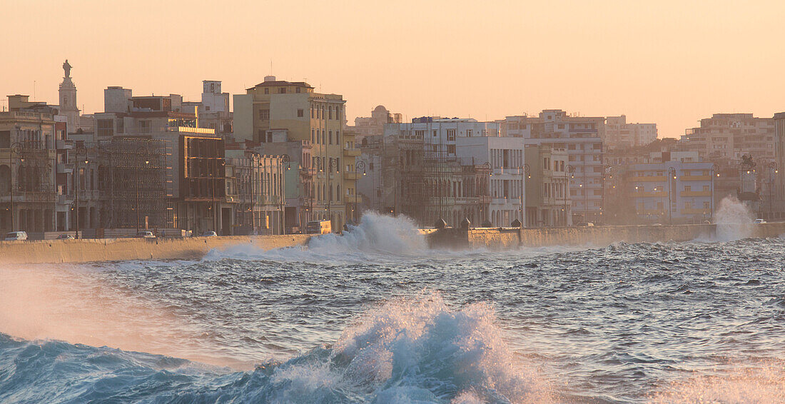 Buildings along The Malecon bathed in soft evening sunlight with large waves crashing against the sea wall, The Malecon, Havana, Cuba, West Indies, Caribbean, Central America