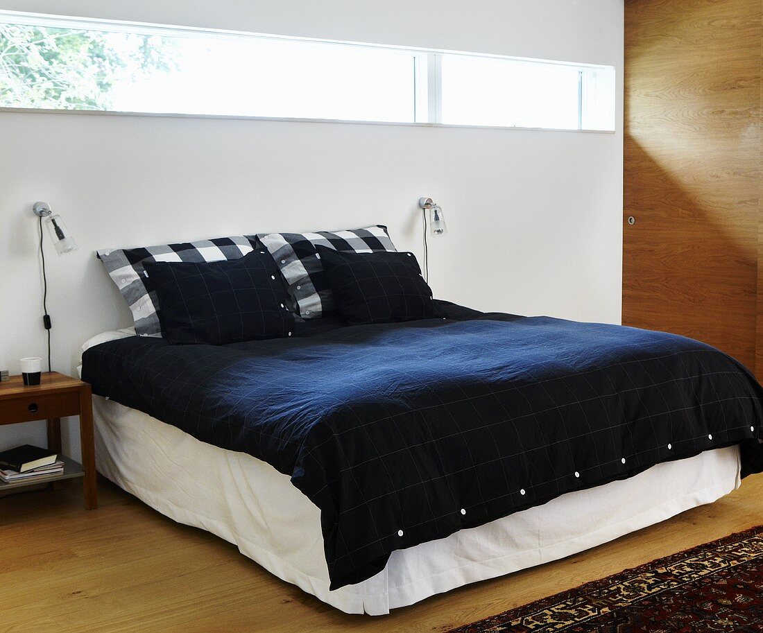Doppelbett mit schwarzer Bettwäsche und Oberlichtstreifen in Wand